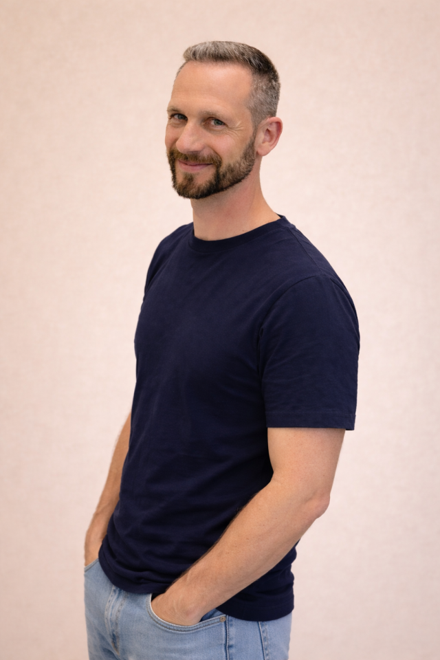 Professional studio portrait placeholder of male physiotherapist, navy-blue clinic uniform, bright clean clinic interior, soft daylight, friendly smile, head and shoulders, subtle bokeh background, accents matching #0b1f3a